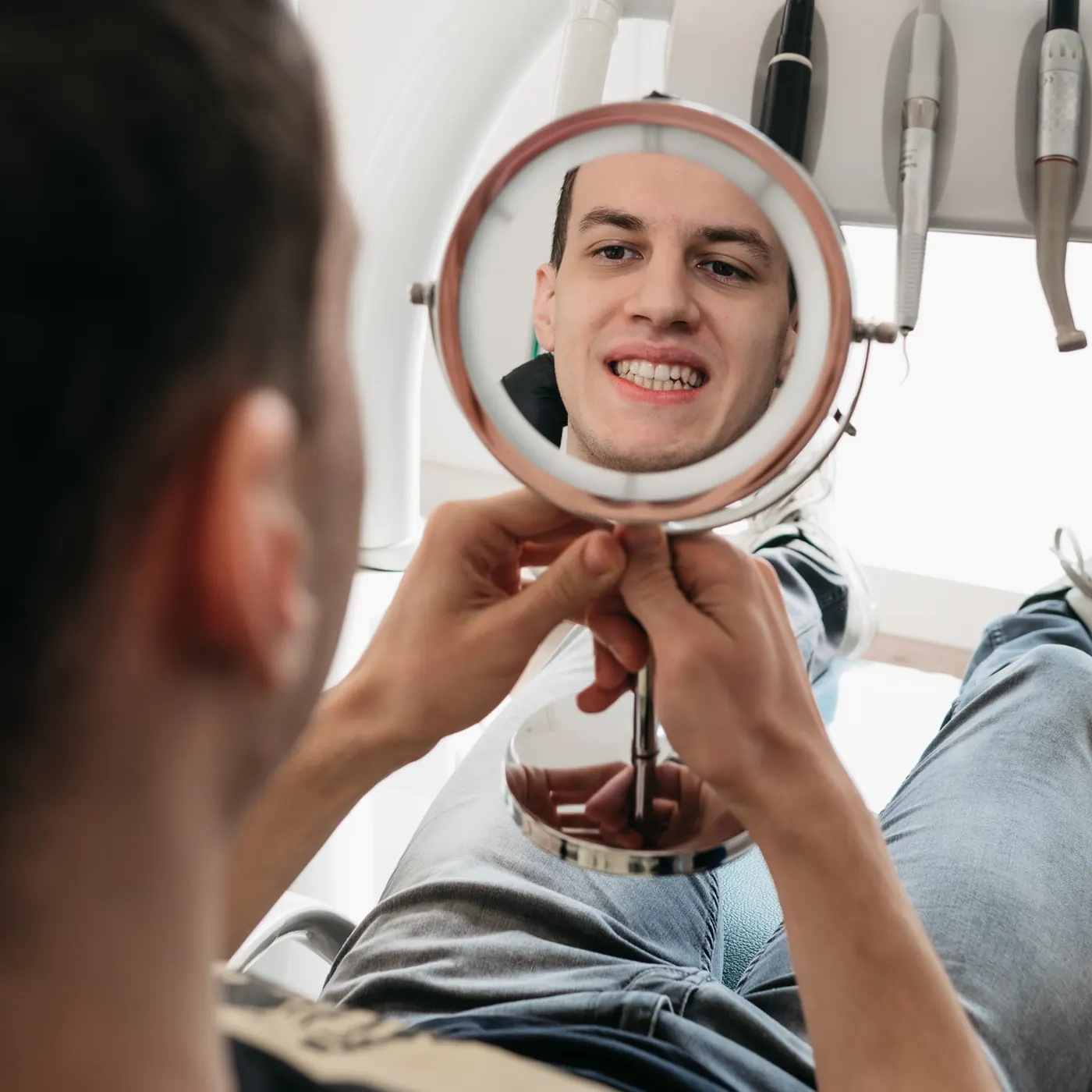 Zadovoljan pacijent gleda u ogledalo nakon stomatološkog tretmana u Dental Centar Apex
